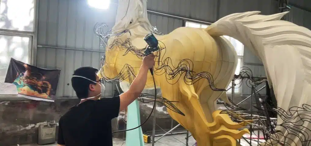 A worker is applying color to a Chinese mythological monster lantern.