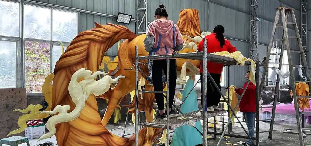 The workers are applying the silk covering to the large animal lantern using the traditional Zigong craftsmanship.